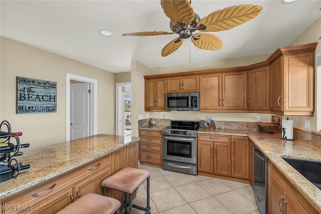 kitchen with light tile patterned floors, light stone countertops, appliances with stainless steel finishes, and brown cabinetry