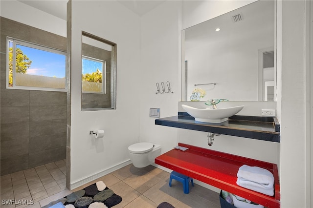 bathroom featuring tile patterned flooring, visible vents, toilet, a tile shower, and a sink