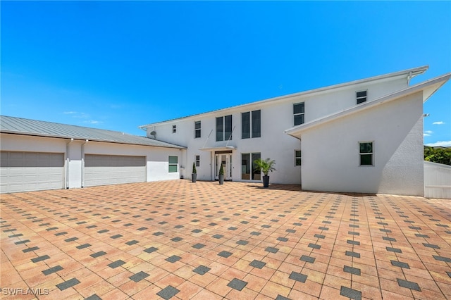 view of front facade featuring an attached garage, metal roof, driveway, and stucco siding