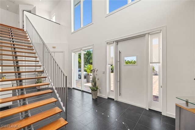 foyer entrance with dark tile patterned floors, stairway, baseboards, and a towering ceiling