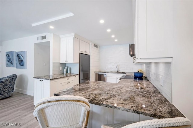 kitchen featuring visible vents, a sink, white cabinetry, stainless steel appliances, and light stone countertops