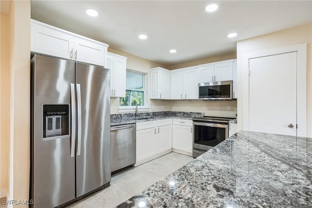 kitchen with stone counters, white cabinets, appliances with stainless steel finishes, and a sink