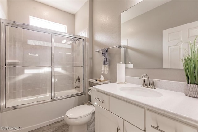 bathroom with bath / shower combo with glass door, wood finished floors, vanity, and toilet