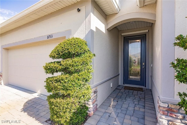 view of exterior entry featuring stucco siding, an attached garage, and driveway