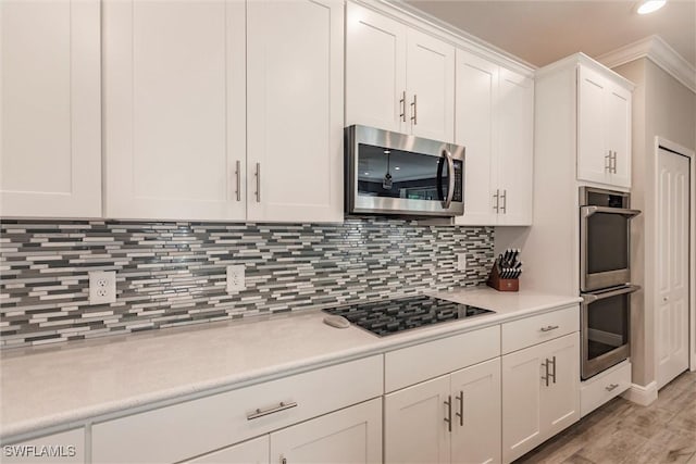 kitchen with light wood-style flooring, stainless steel appliances, light countertops, white cabinets, and tasteful backsplash