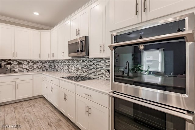 kitchen with decorative backsplash, light countertops, white cabinets, stainless steel microwave, and black electric cooktop