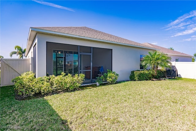 rear view of property featuring a yard, a sunroom, stucco siding, and fence