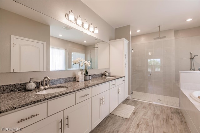 bathroom featuring double vanity, a stall shower, tiled tub, and a sink