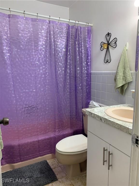 full bathroom with tile patterned floors, tile walls, toilet, vanity, and shower / tub combo with curtain