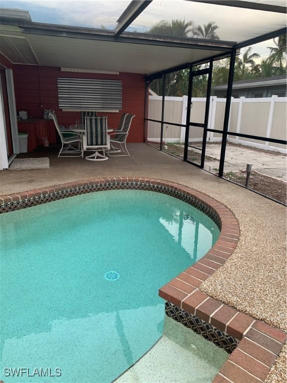 view of pool with glass enclosure, a patio, and fence