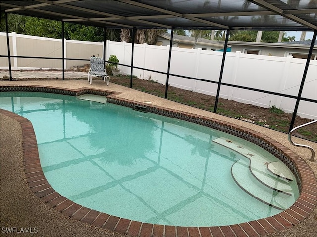 view of swimming pool featuring glass enclosure, a patio area, a fenced backyard, and a fenced in pool