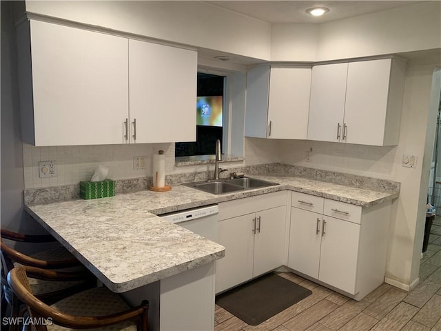 kitchen with a peninsula, white cabinetry, light countertops, and a sink