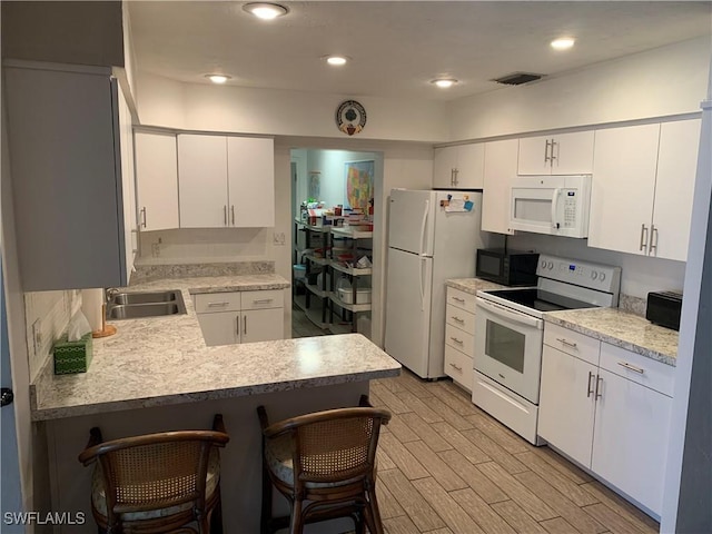 kitchen featuring white appliances, a breakfast bar area, light countertops, a sink, and visible vents