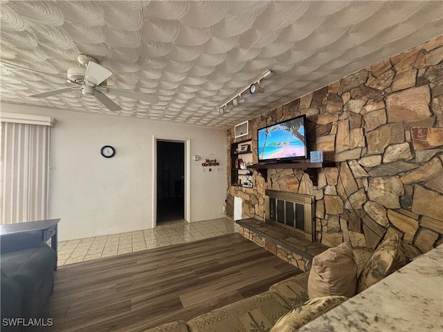 living room with ceiling fan, track lighting, a stone fireplace, visible vents, and wood finished floors