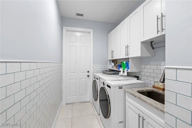 laundry area with washing machine and clothes dryer, visible vents, light tile patterned floors, cabinet space, and tile walls