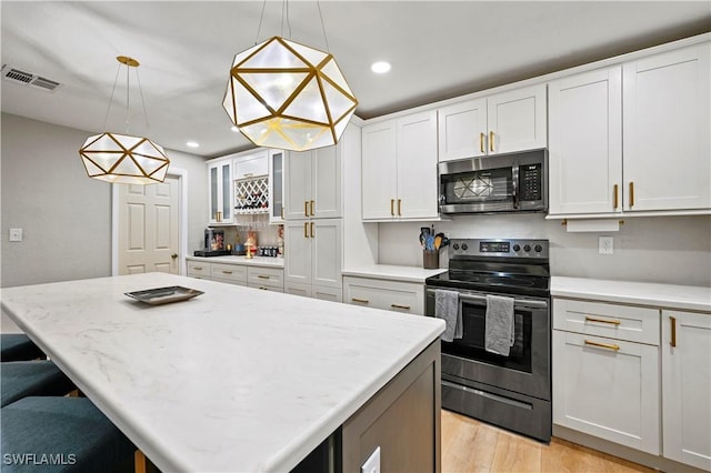 kitchen featuring visible vents, a kitchen island, light wood-type flooring, appliances with stainless steel finishes, and white cabinets