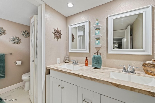 bathroom with double vanity, toilet, marble finish floor, and a sink