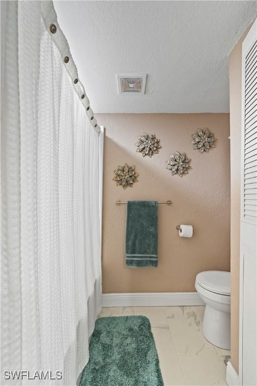 full bathroom featuring visible vents, toilet, marble finish floor, a textured ceiling, and baseboards