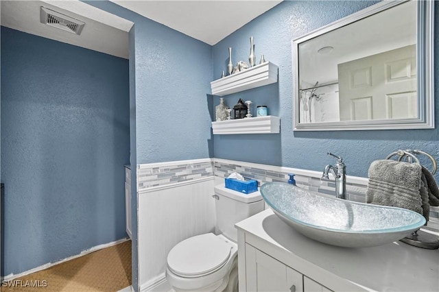 full bath featuring vanity, a wainscoted wall, visible vents, toilet, and a textured wall
