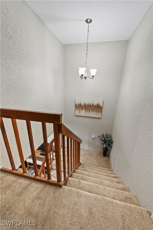 stairway with carpet, an inviting chandelier, and a textured wall