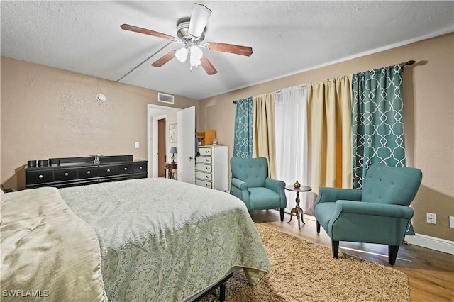 bedroom featuring visible vents, baseboards, wood finished floors, a textured ceiling, and a ceiling fan