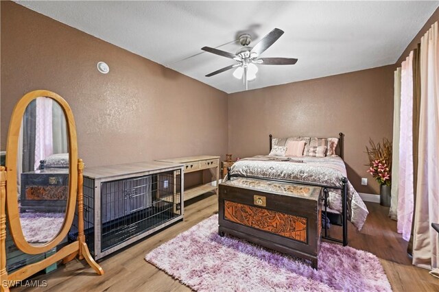 bedroom with wood finished floors, baseboards, a textured wall, and ceiling fan