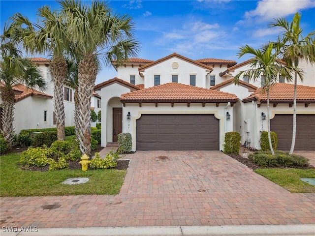 mediterranean / spanish home featuring a garage, decorative driveway, stucco siding, and a tile roof