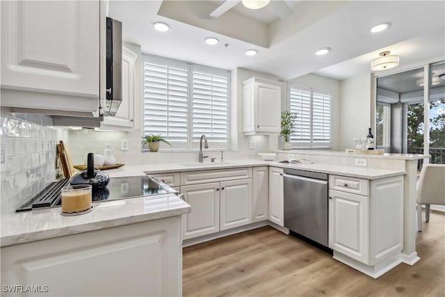 kitchen with stainless steel dishwasher, a sink, a peninsula, white cabinets, and backsplash