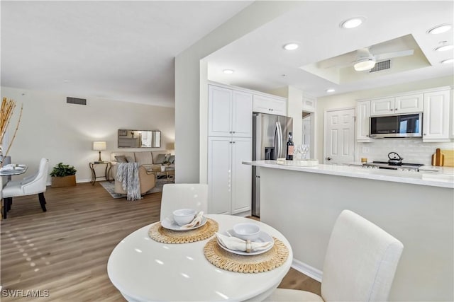 dining area with light wood-style flooring, recessed lighting, baseboards, and a raised ceiling