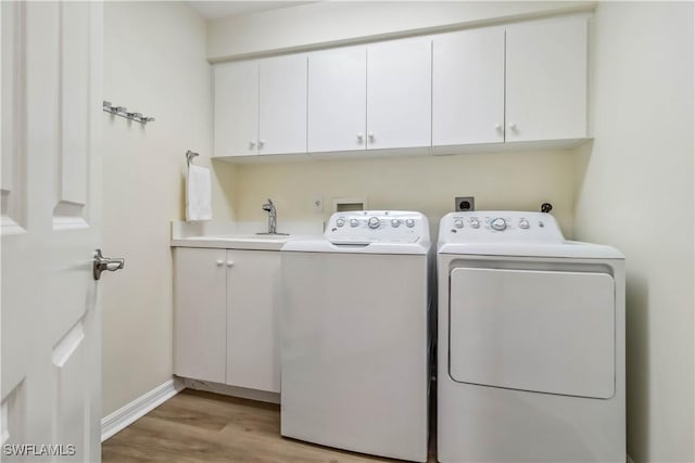 clothes washing area with cabinet space, light wood-style flooring, washing machine and dryer, and baseboards