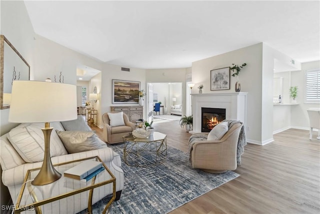 living room featuring wood finished floors, a glass covered fireplace, and baseboards