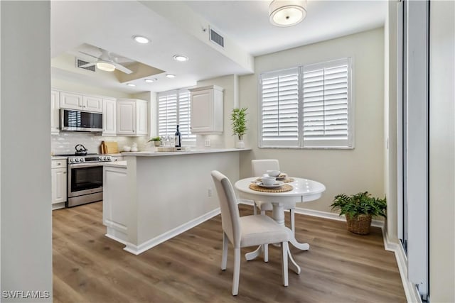 kitchen with stainless steel appliances, light wood finished floors, white cabinetry, ceiling fan, and decorative backsplash
