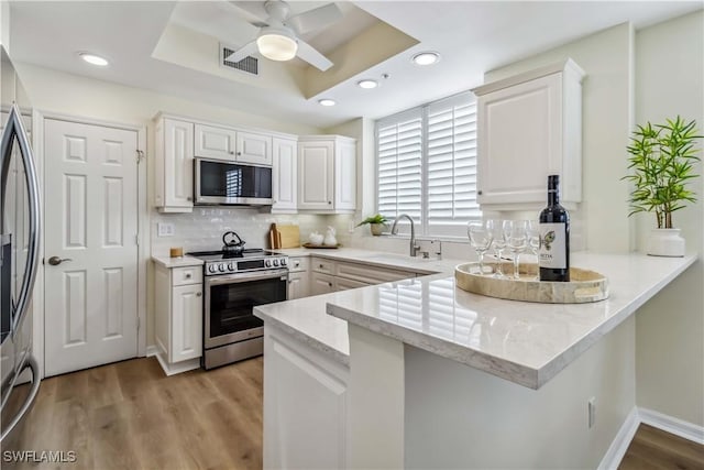 kitchen with appliances with stainless steel finishes, a sink, a peninsula, white cabinets, and light stone countertops