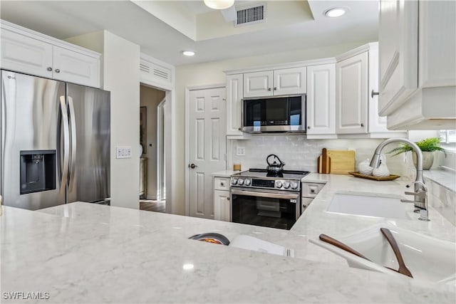 kitchen featuring stainless steel appliances, white cabinets, a sink, light stone countertops, and recessed lighting