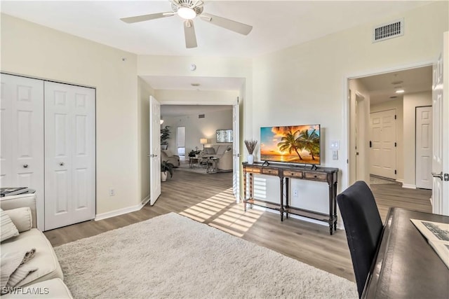 living area featuring wood finished floors, an office area, ceiling fan, and baseboards