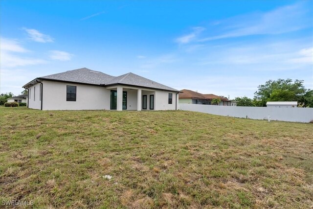 back of property featuring stucco siding, a lawn, and fence