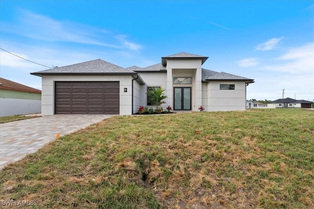 prairie-style house with stucco siding, driveway, french doors, a front yard, and a garage
