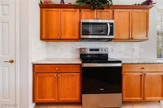 kitchen with stainless steel appliances, backsplash, light tile patterned floors, and light stone counters