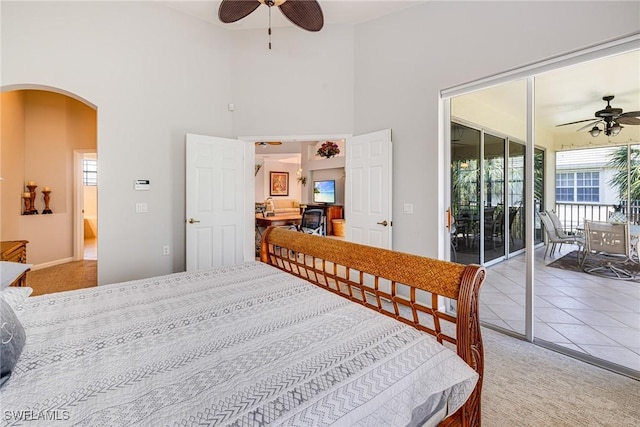 bedroom featuring access to exterior, arched walkways, ceiling fan, light carpet, and a high ceiling