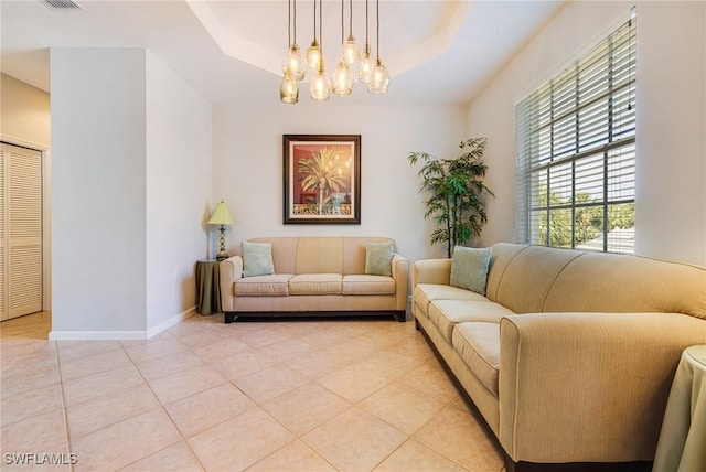 living room featuring a raised ceiling, a chandelier, light tile patterned flooring, and baseboards