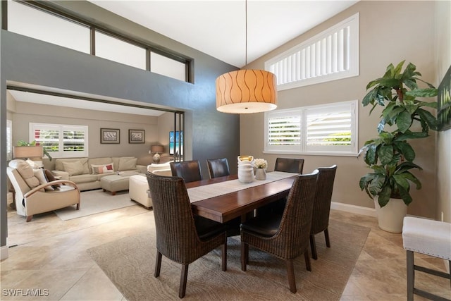 dining space with light tile patterned flooring, baseboards, and a high ceiling