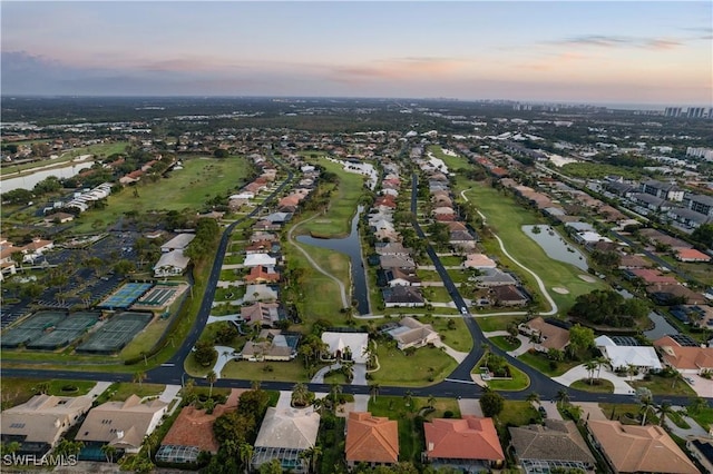 aerial view at dusk featuring view of golf course, a residential view, and a water view