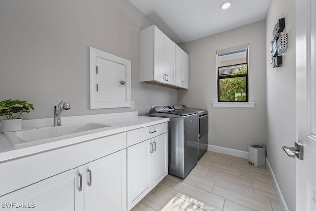 washroom with a sink, cabinet space, baseboards, and separate washer and dryer