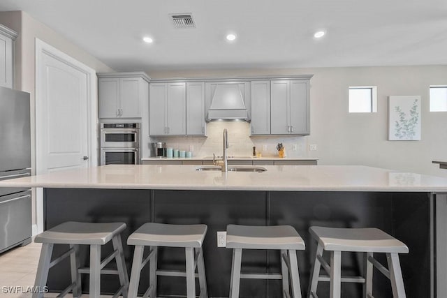 kitchen with visible vents, stainless steel double oven, gray cabinets, a sink, and tasteful backsplash