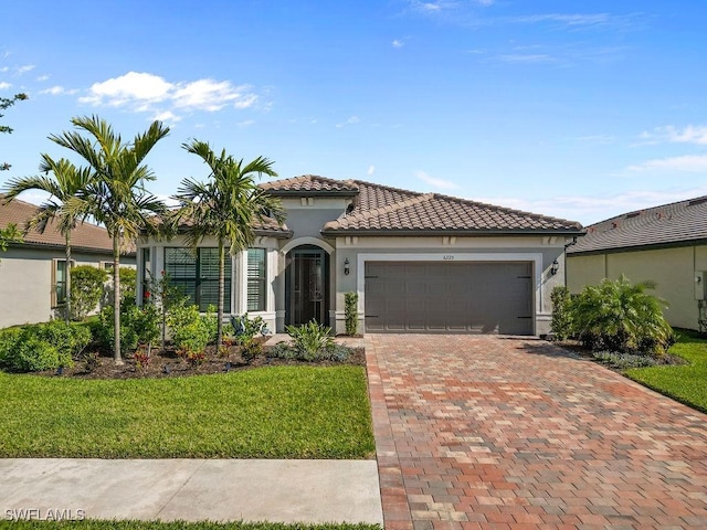 mediterranean / spanish home featuring a front yard, stucco siding, a garage, a tiled roof, and decorative driveway