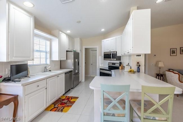 7520 Firenze Ln, Naples, FL 34114 - kitchen with a breakfast bar, a peninsula, light tile patterned flooring, white cabinets, and appliances with stainless steel finishes