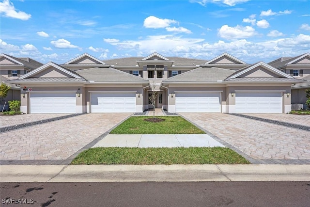 view of front of property with stucco siding, a tile roof, decorative driveway, cooling unit, and a garage