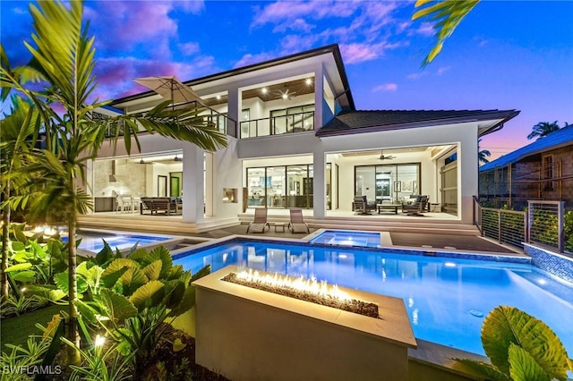 rear view of house featuring an in ground hot tub, a ceiling fan, stucco siding, a balcony, and outdoor dining area
