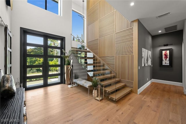 foyer with stairs, a high ceiling, wood finished floors, baseboards, and visible vents