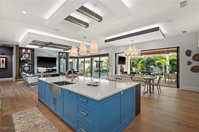 kitchen with wood finished floors, blue cabinetry, a sink, open floor plan, and pendant lighting